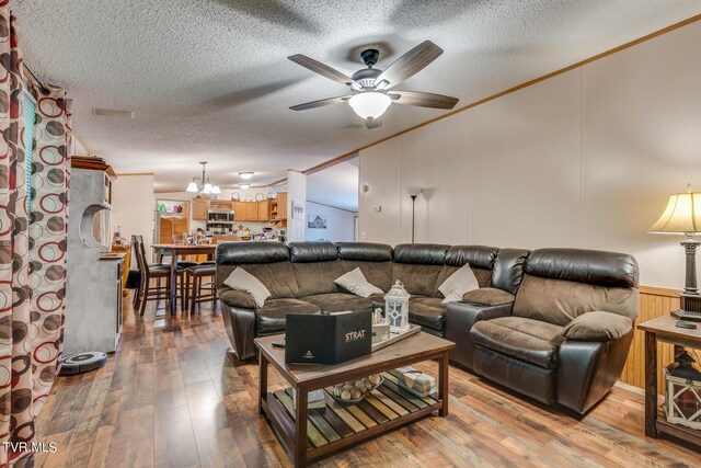 living room featuring ceiling fan with notable chandelier, a textured ceiling, crown molding, lofted ceiling, and hardwood / wood-style flooring