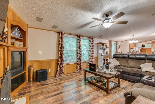 living room with a textured ceiling, ceiling fan with notable chandelier, ornamental molding, and hardwood / wood-style flooring