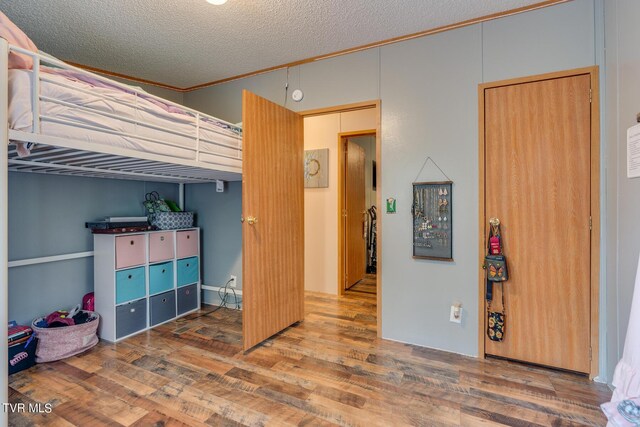 bedroom with a textured ceiling, wood-type flooring, and ornamental molding