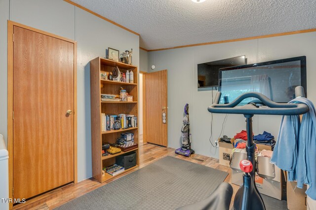 exercise area with a textured ceiling, light hardwood / wood-style flooring, crown molding, and lofted ceiling