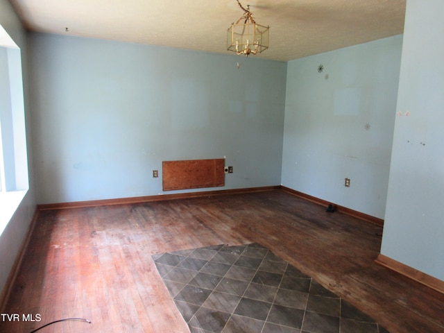 unfurnished room featuring an inviting chandelier, a textured ceiling, and dark hardwood / wood-style floors