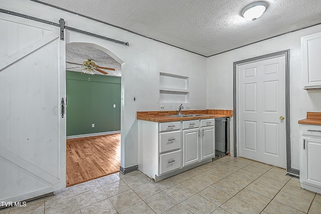 kitchen with a textured ceiling, white cabinets, a barn door, wooden counters, and ceiling fan