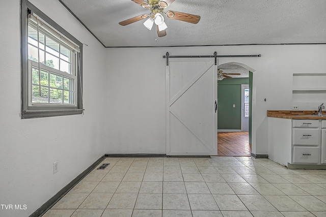 tiled spare room with a textured ceiling, ceiling fan, sink, and a barn door