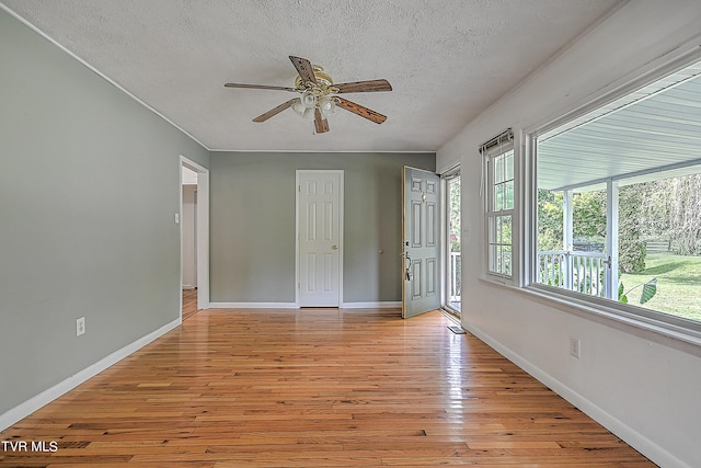 interior space with light wood-type flooring, multiple windows, ceiling fan, and a textured ceiling