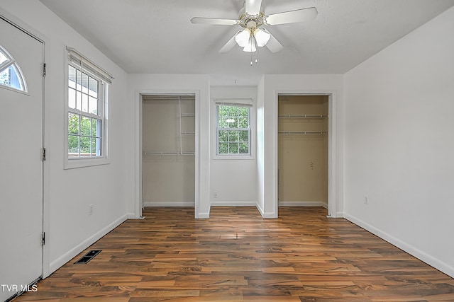 unfurnished bedroom featuring multiple windows, two closets, ceiling fan, and dark wood-type flooring