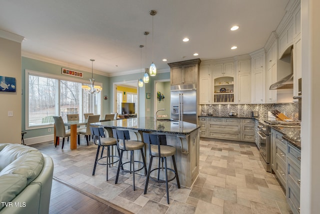 kitchen with hanging light fixtures, decorative backsplash, high end appliances, dark stone counters, and a kitchen island with sink