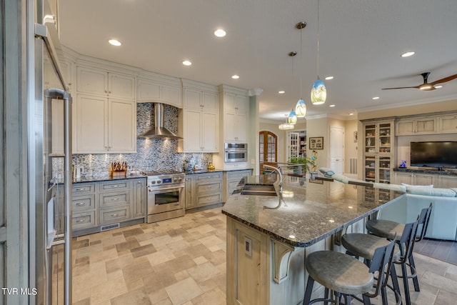 kitchen with wall chimney exhaust hood, pendant lighting, stainless steel appliances, ceiling fan, and sink