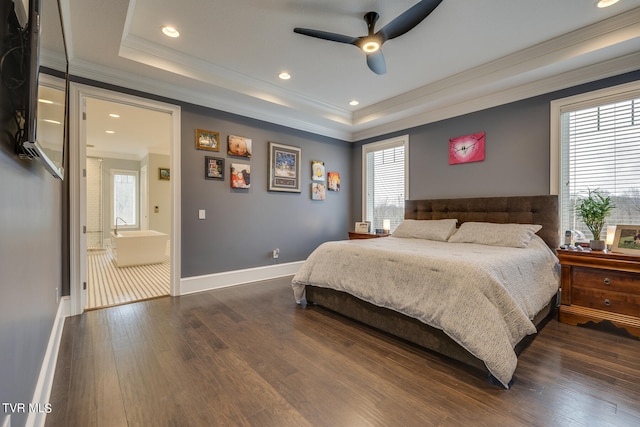 bedroom with a tray ceiling, dark hardwood / wood-style floors, connected bathroom, crown molding, and ceiling fan