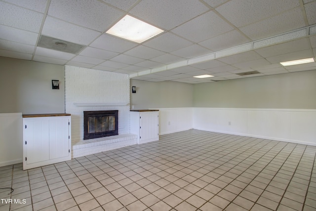 unfurnished living room featuring a drop ceiling, light tile patterned floors, and a brick fireplace