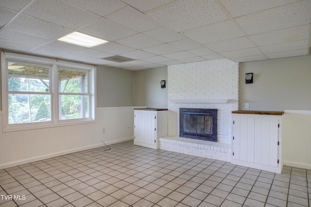 unfurnished living room with a paneled ceiling, a fireplace, and light tile patterned floors