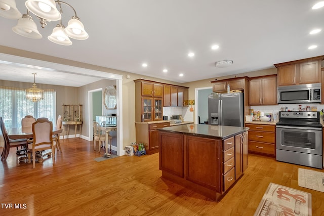 kitchen with pendant lighting, light wood-type flooring, a center island, an inviting chandelier, and appliances with stainless steel finishes