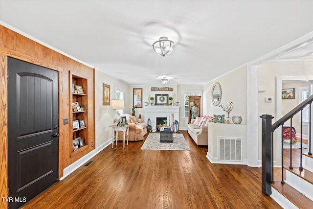 living room with crown molding, wooden walls, dark hardwood / wood-style flooring, and built in features