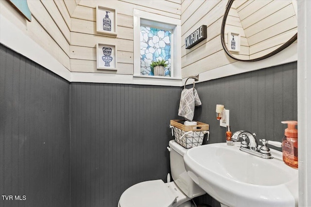 bathroom with wood walls, toilet, and sink