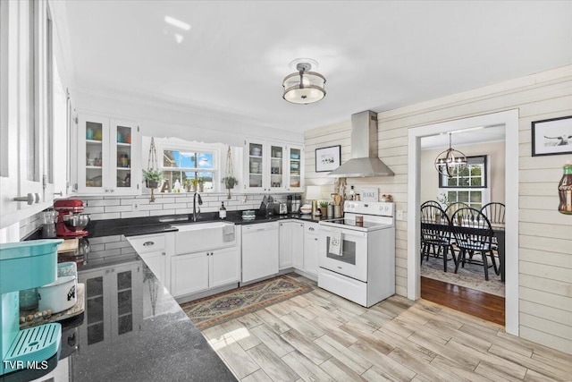 kitchen with white appliances, white cabinets, wall chimney range hood, and plenty of natural light