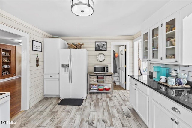 kitchen featuring light wood-type flooring, wood walls, white refrigerator with ice dispenser, and white cabinets