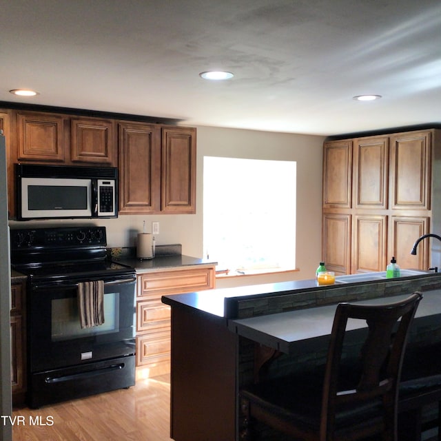 kitchen with electric range, a kitchen breakfast bar, and light hardwood / wood-style floors