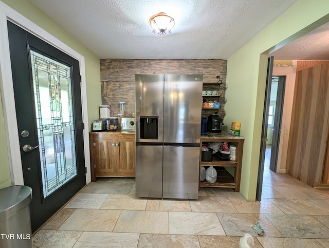 kitchen with wooden walls, stainless steel refrigerator with ice dispenser, and a textured ceiling