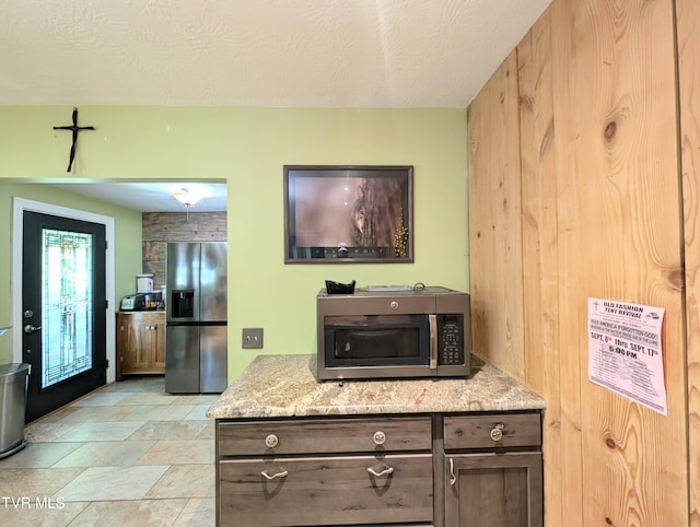 kitchen with a textured ceiling, dark brown cabinets, light stone countertops, and stainless steel appliances