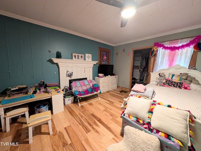 bedroom featuring ceiling fan, wood-type flooring, a closet, a fireplace, and crown molding