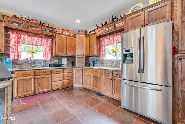 kitchen with light stone countertops, stainless steel fridge, sink, and a healthy amount of sunlight