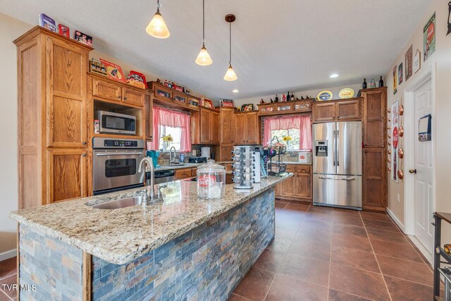 kitchen with light stone counters, sink, decorative light fixtures, appliances with stainless steel finishes, and a center island