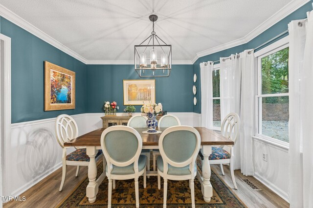 dining room featuring wood-type flooring, a notable chandelier, crown molding, and a textured ceiling