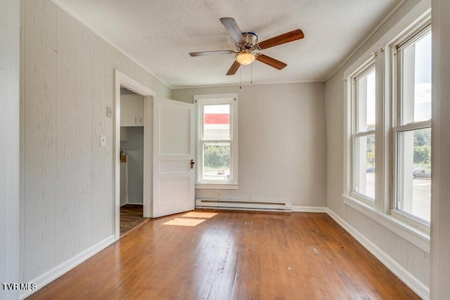 empty room with baseboard heating, a healthy amount of sunlight, hardwood / wood-style floors, and a textured ceiling