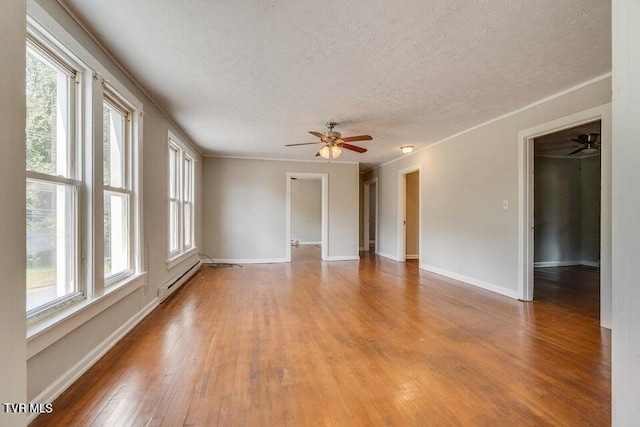 empty room featuring a baseboard heating unit, baseboards, light wood-type flooring, and a textured ceiling