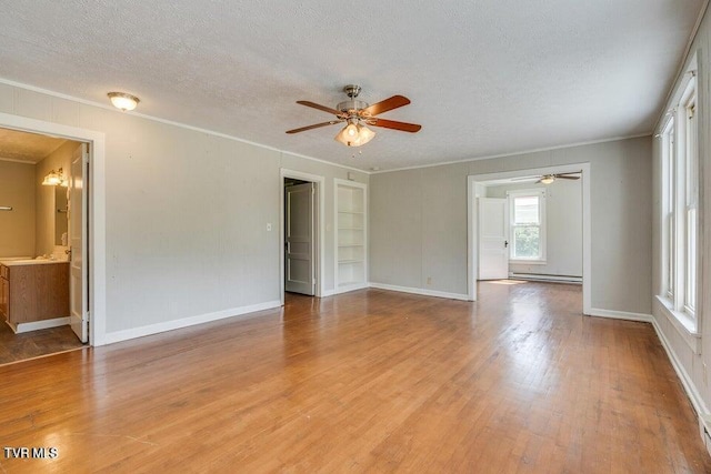 spare room featuring light wood-style flooring, a baseboard heating unit, a textured ceiling, crown molding, and ceiling fan