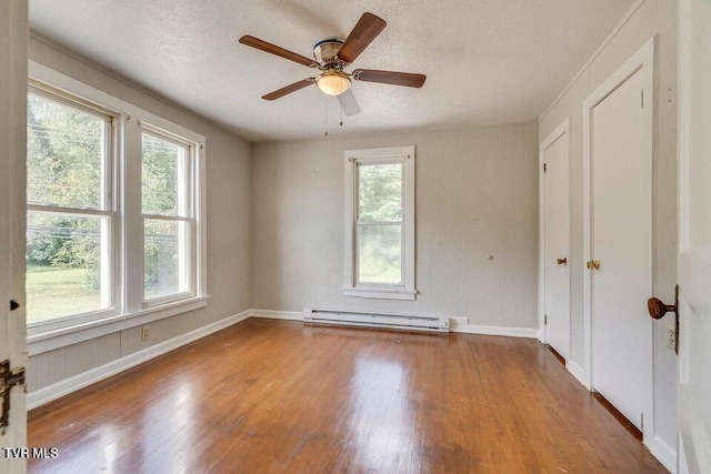 unfurnished room with a textured ceiling, a baseboard heating unit, baseboards, and wood finished floors