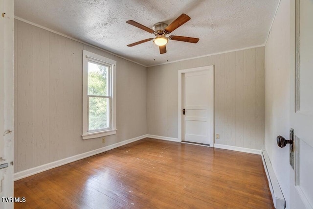 empty room with a baseboard heating unit, hardwood / wood-style flooring, a textured ceiling, and ornamental molding