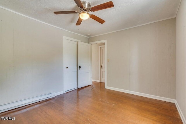 empty room featuring a textured ceiling, baseboard heating, crown molding, and light wood finished floors