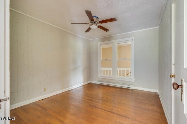 spare room with crown molding, wood finished floors, baseboards, and a baseboard radiator