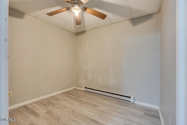 empty room featuring baseboards, ceiling fan, wood finished floors, a paneled ceiling, and a baseboard radiator