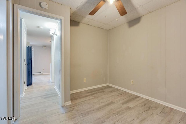 unfurnished room with ceiling fan, a baseboard heating unit, light wood-type flooring, and a paneled ceiling