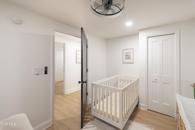 bedroom with ceiling fan, a closet, a nursery area, and light wood-type flooring