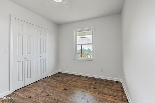 unfurnished bedroom with a textured ceiling, dark hardwood / wood-style flooring, ceiling fan, and a closet