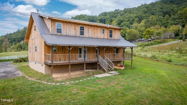 view of front of property with covered porch, a front yard, a forest view, and metal roof