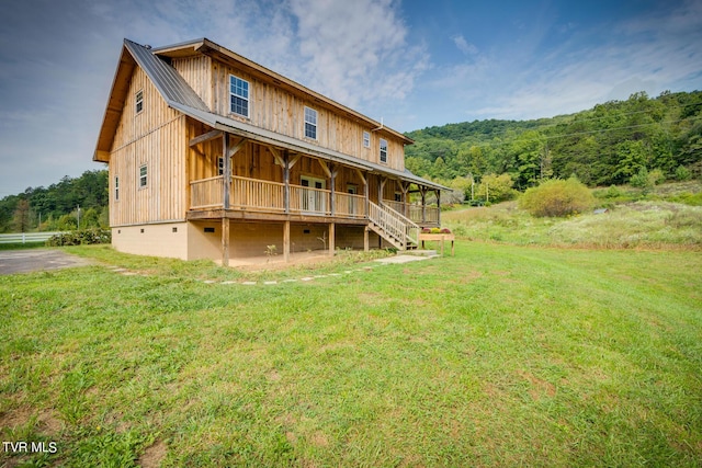 back of property featuring a lawn, metal roof, and a forest view