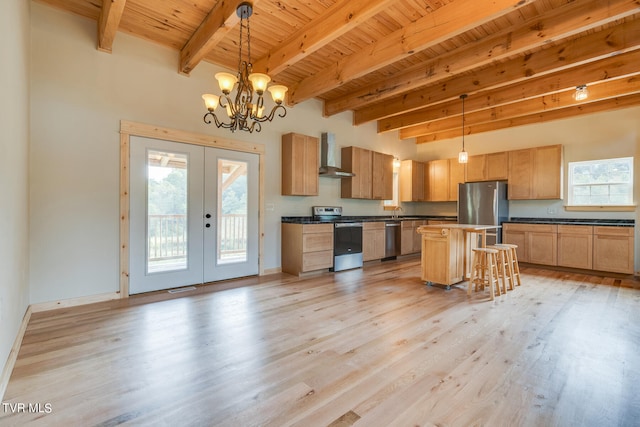 kitchen with french doors, a center island, appliances with stainless steel finishes, pendant lighting, and wall chimney range hood