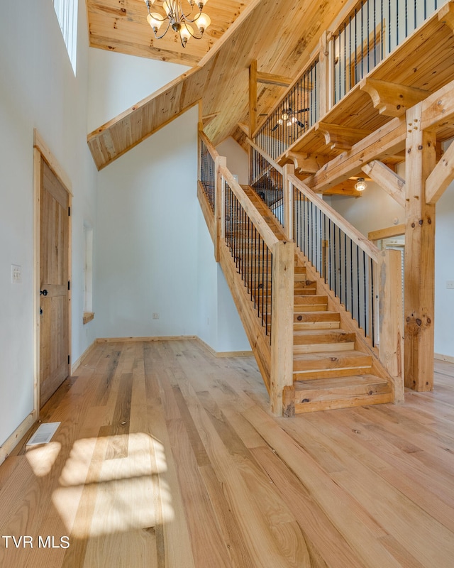 stairs featuring an inviting chandelier, hardwood / wood-style flooring, high vaulted ceiling, and wooden ceiling