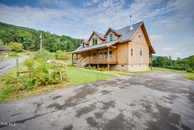 view of front facade featuring metal roof, a wooded view, crawl space, a front yard, and covered porch