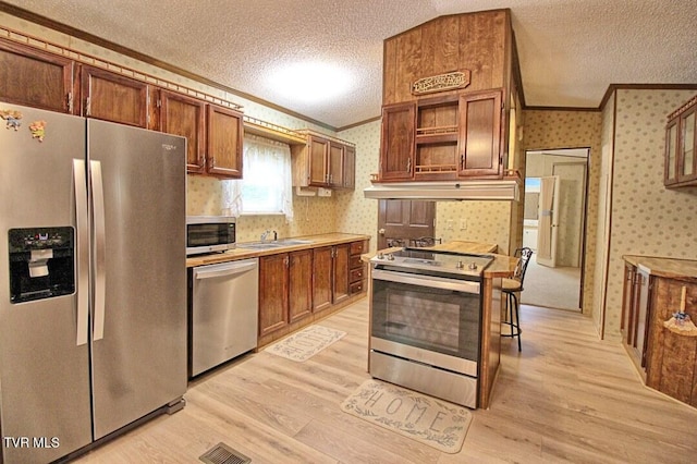 kitchen with appliances with stainless steel finishes, crown molding, a textured ceiling, and light wood-type flooring