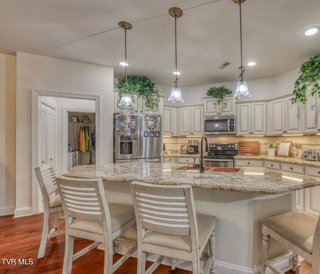 kitchen featuring appliances with stainless steel finishes, dark hardwood / wood-style flooring, a center island with sink, and pendant lighting