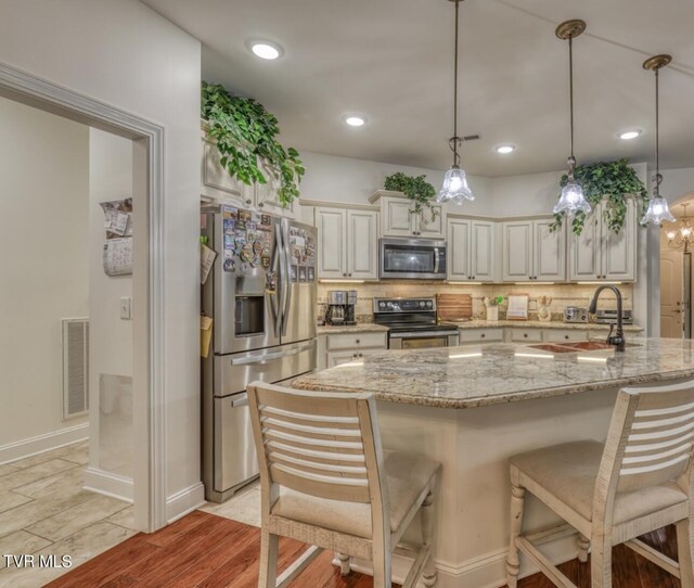 kitchen with stainless steel appliances, light stone counters, light hardwood / wood-style flooring, backsplash, and decorative light fixtures