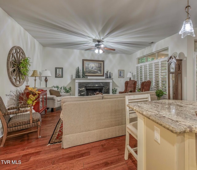 living room with a premium fireplace, ceiling fan, and wood-type flooring