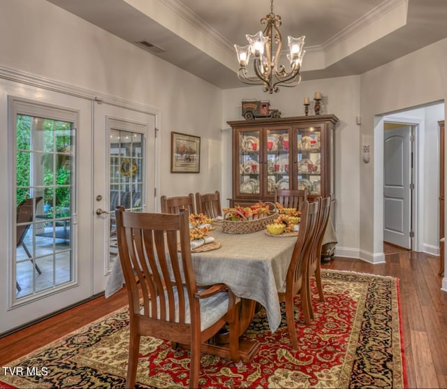 dining space with french doors, crown molding, hardwood / wood-style flooring, a tray ceiling, and a chandelier