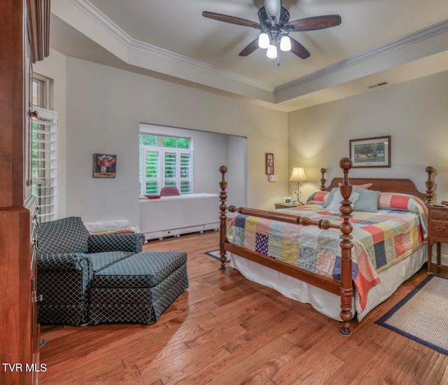 bedroom with ceiling fan, a baseboard radiator, a raised ceiling, light wood-type flooring, and ornamental molding