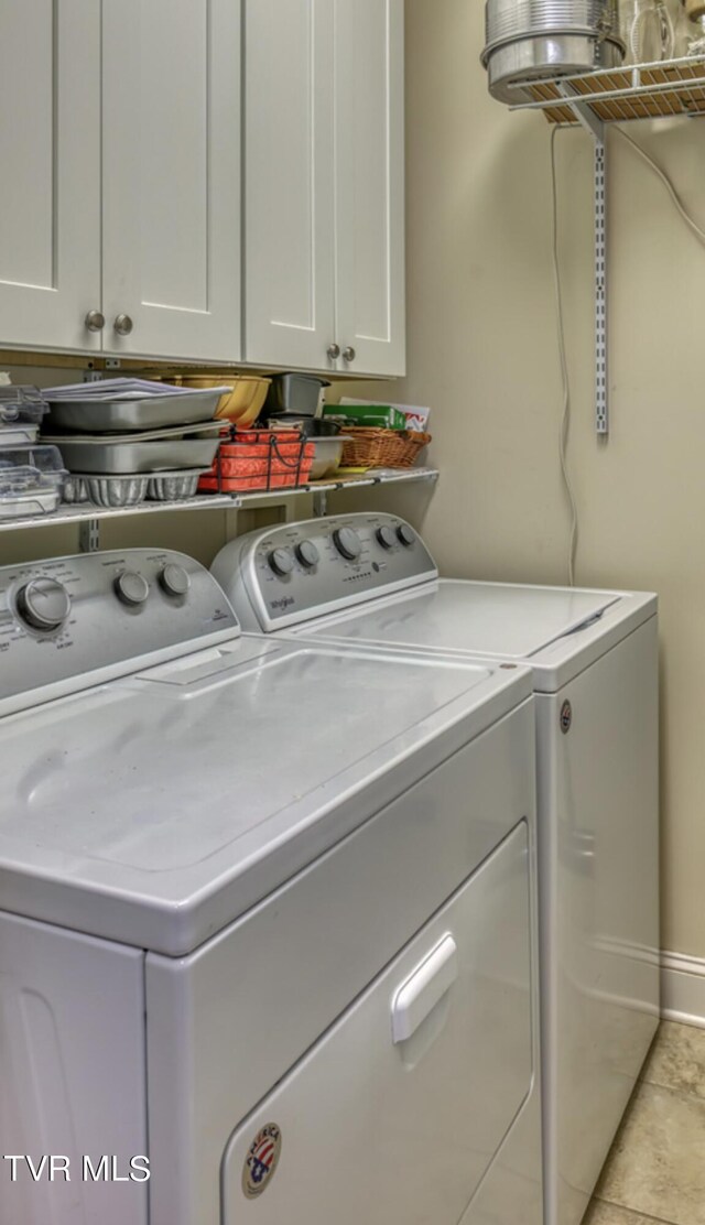 laundry room featuring washing machine and clothes dryer, light tile patterned floors, and cabinets