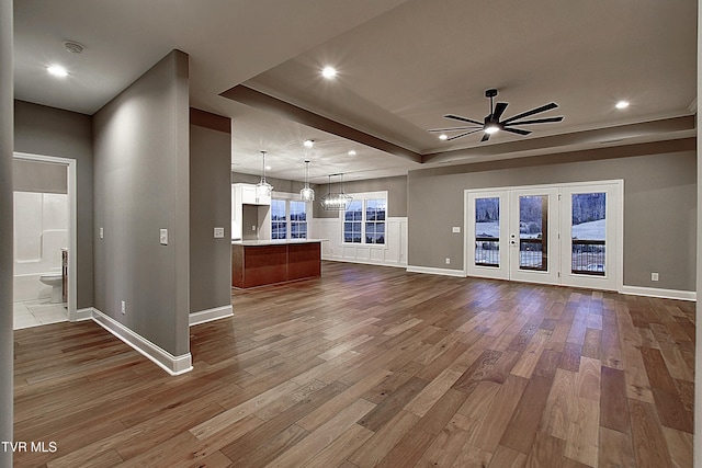 unfurnished living room with a tray ceiling, ceiling fan with notable chandelier, and hardwood / wood-style flooring